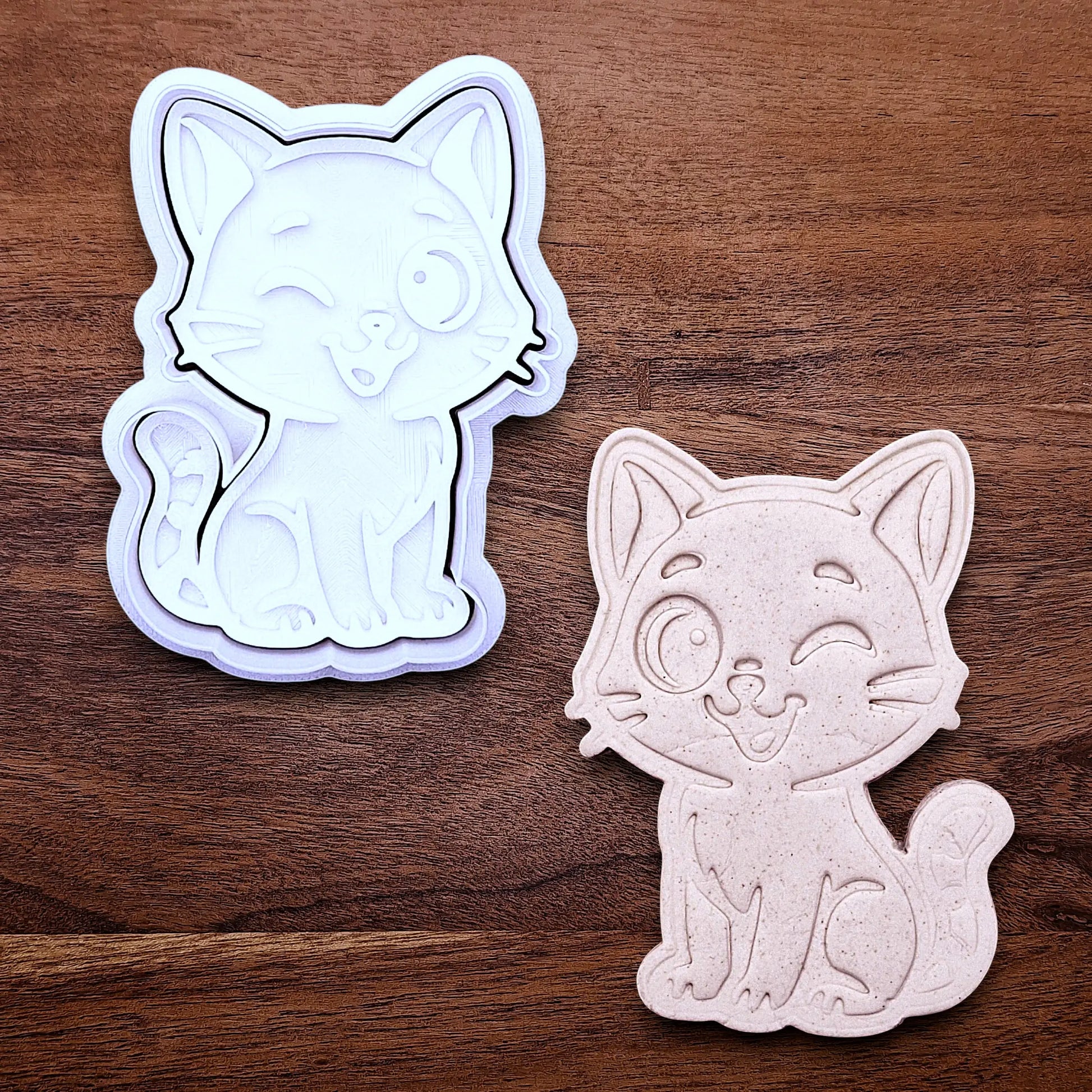 Winking cat cookie cutter and stamp alongside a dough cutout and imprint, great for creating detailed, cat-themed cookies, fondant pieces, or party treats for birthdays, parties and craft projects.