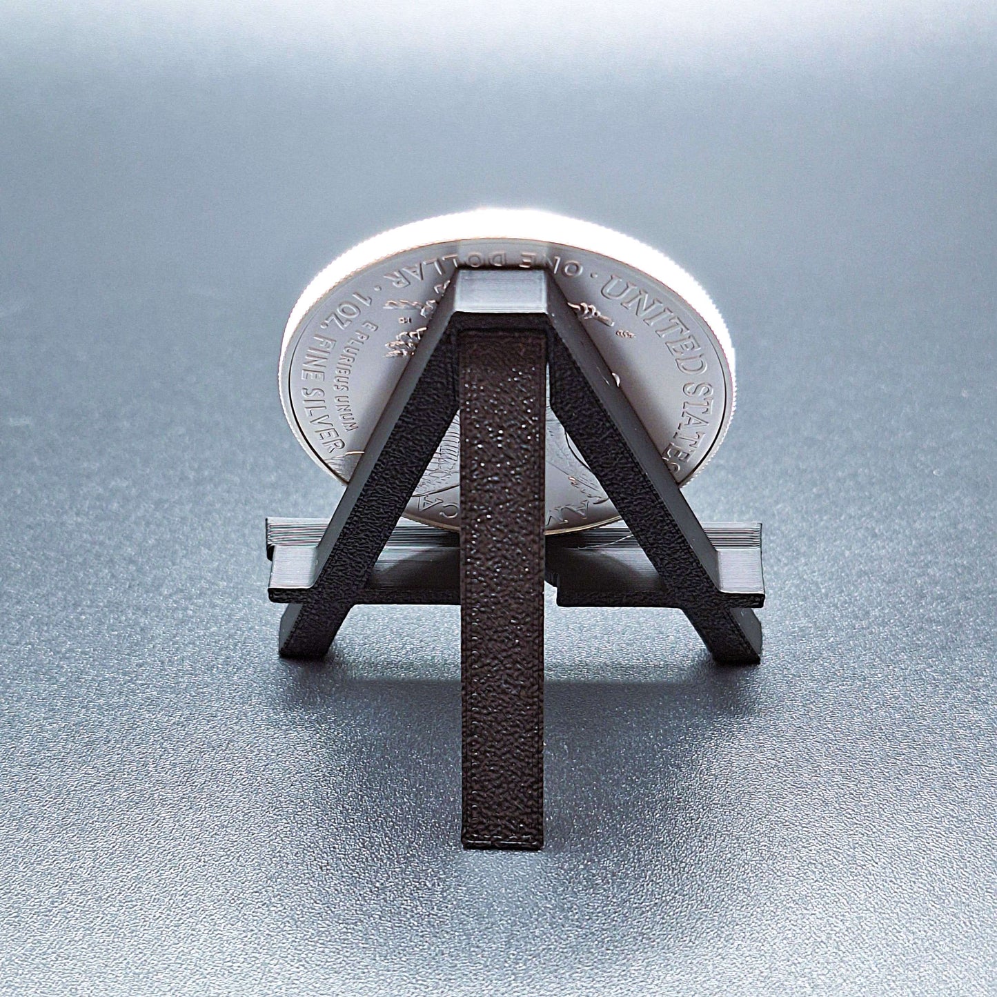 Reverse side of mini foldable easel, shown holding an American Silver Eagle, showcasing the foldable arm and sturdy design.