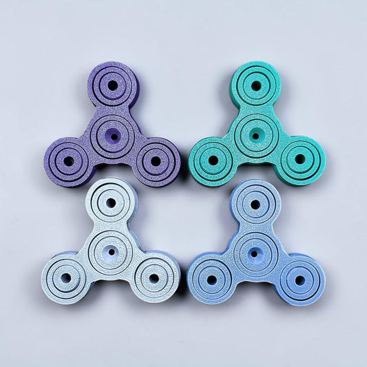 Four fidget spinners in purple, green, white, and blue on a light gray background