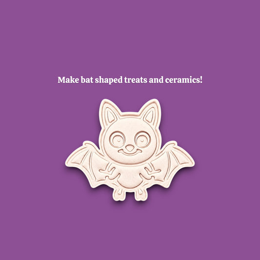 A cute bat-shaped cookie cutter mold shown on a solid purple background with white text that reads 'Make fun bat shaped treats, ceramics and ornaments!'. The bat is off-white with a light pinkish-beige undertone and a subtle drop shadow.