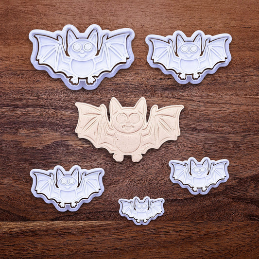 Bat cookie cutters with matching stamps and dough cutout with bat design pressed by cutter and stamp set, showing detailed lines—great for easy Halloween cookie decorating without icing.