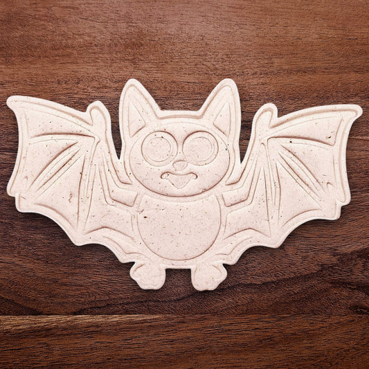 Dough cutout with bat design pressed by cutter and stamp set, showing detailed lines—great for easy Halloween cookie decorating without icing.