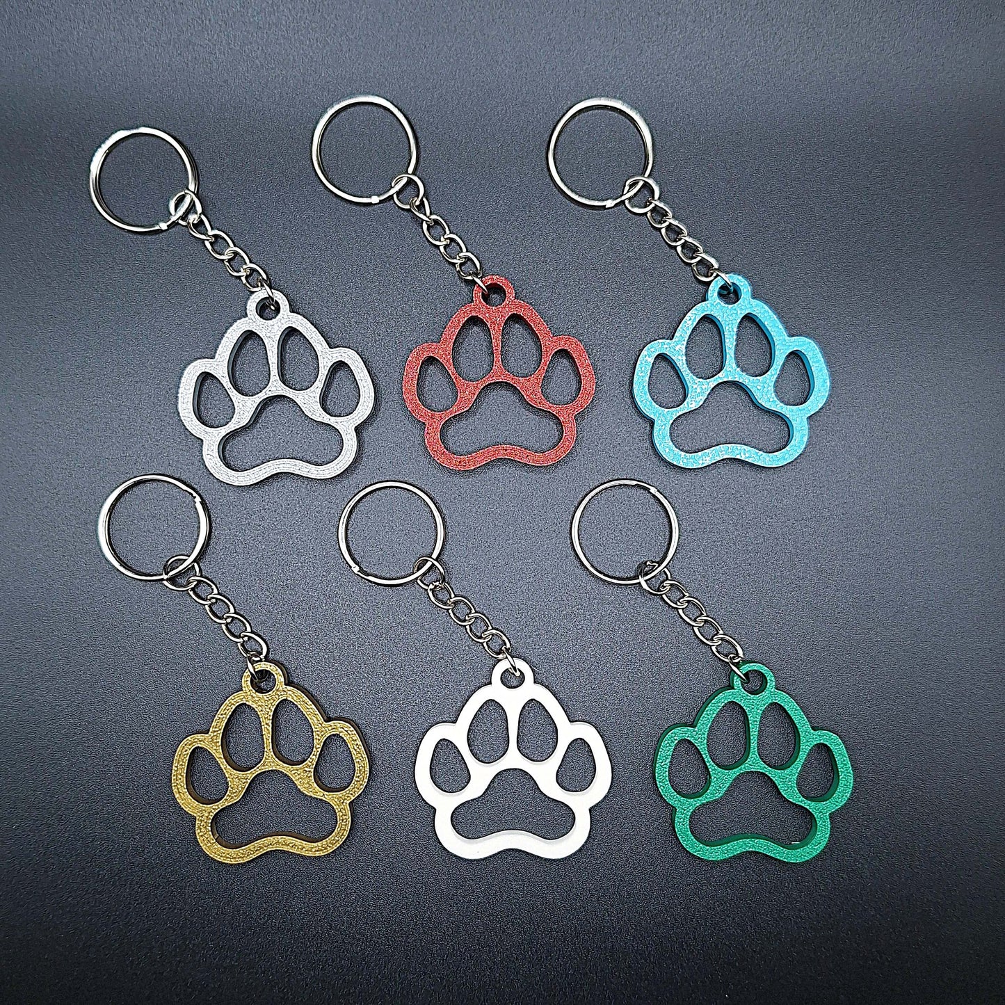 Six paw print keychains in assorted colors, made from biodegradable PLA plastic, perfect for dog moms, cat lovers, or rescue volunteers.
