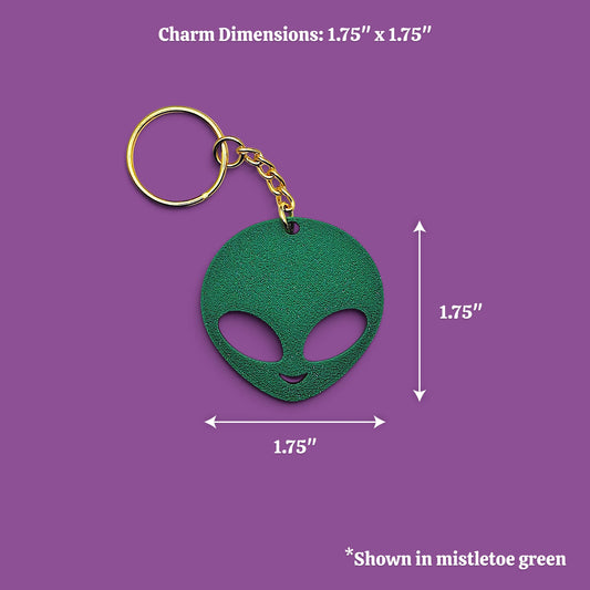 A green alien-head keychain with a gold key ring and chain, shown on a purple background with dimension labels indicating 1.75 inches by 1.75