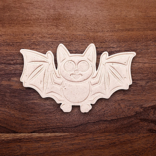Dough cutout with bat design pressed by cutter and stamp set, showing detailed lines—great for easy Halloween cookie decorating without icing.