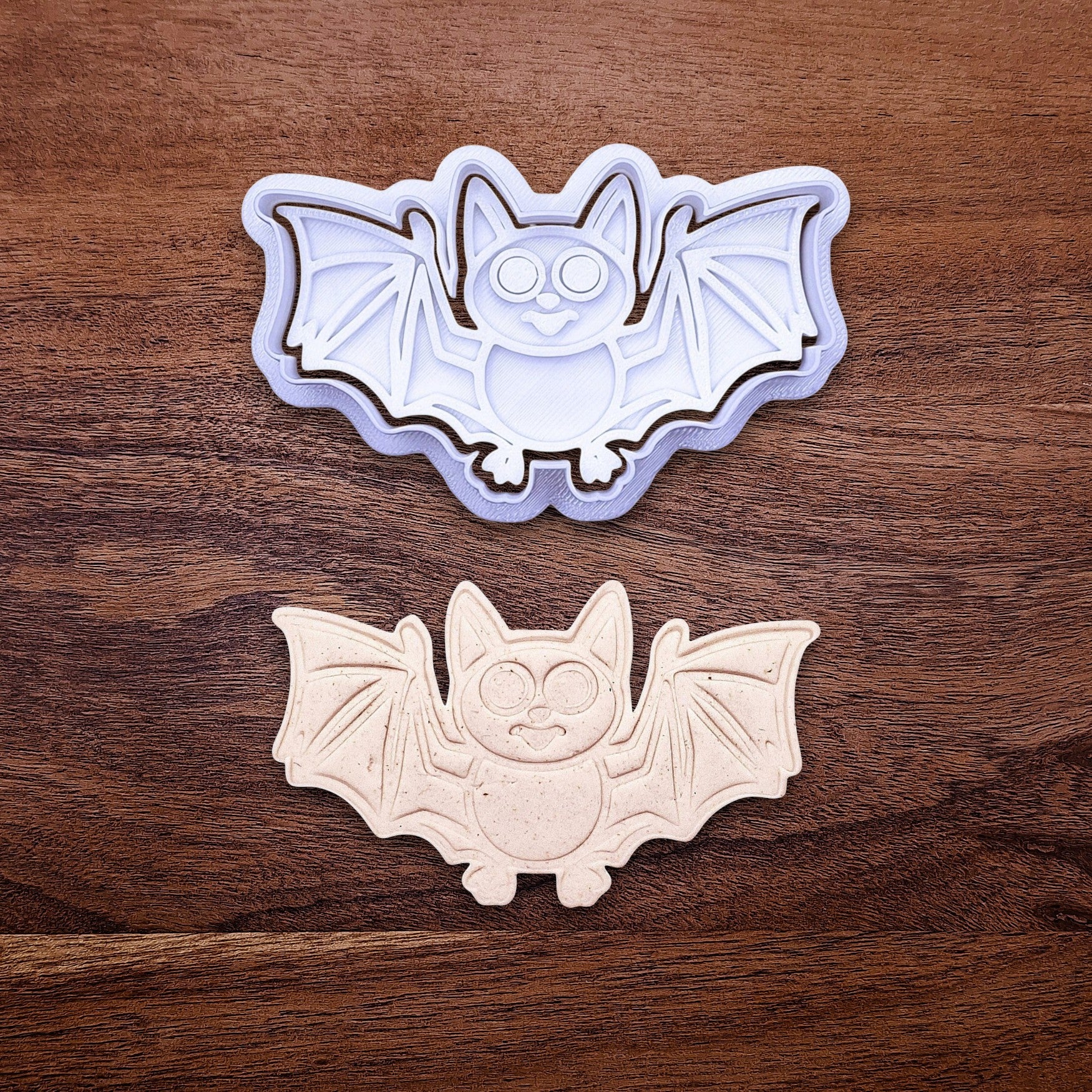 Bat cookie cutter with matching stamp and dough cutout with bat design pressed by cutter and stamp set, showing detailed lines—great for easy Halloween cookie decorating without icing.