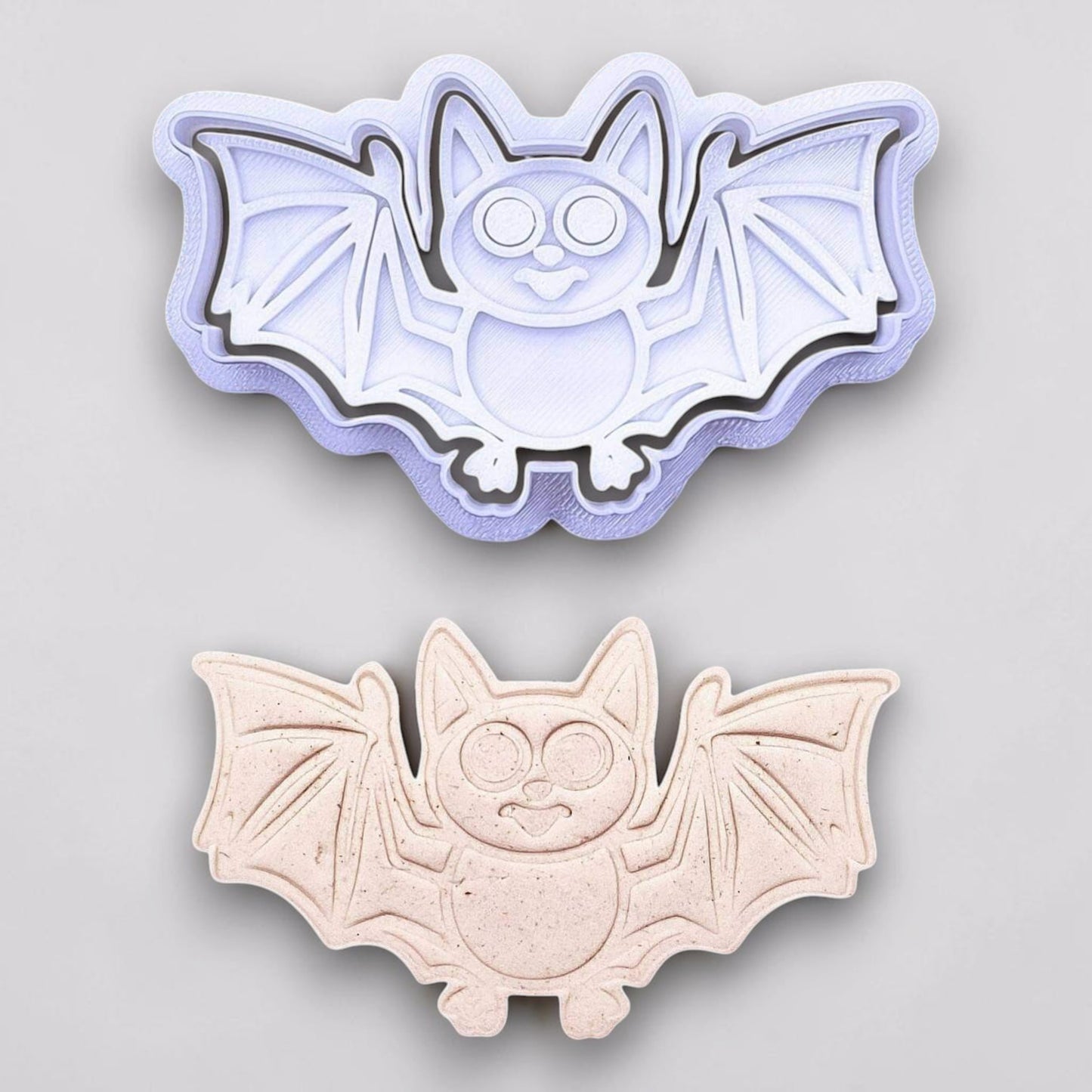 Bat cookie cutter with matching stamp and dough cutout with bat design pressed by cutter and stamp set, showing detailed lines—great for easy Halloween cookie decorating without icing.
