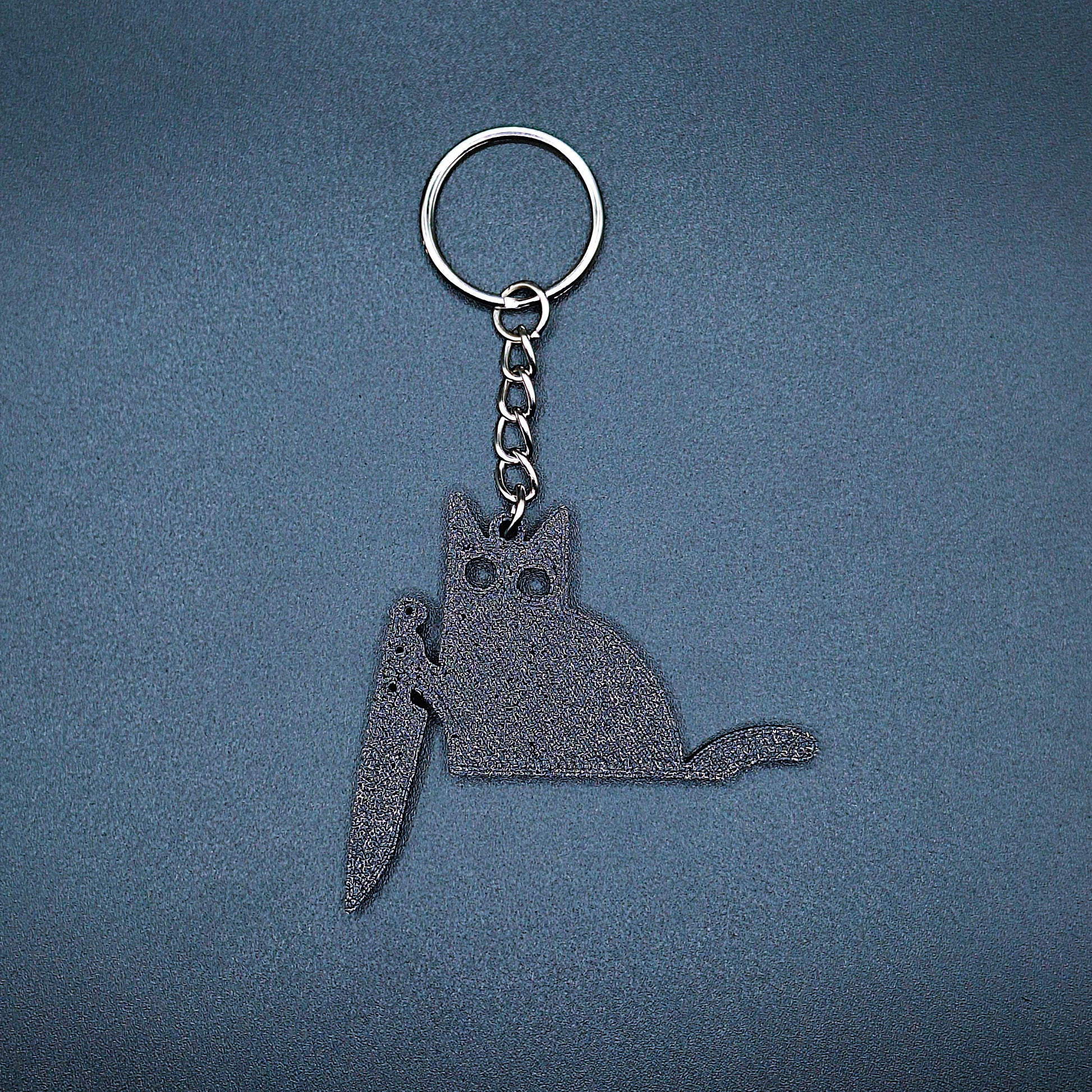 Front view of black cat keychain holding a kitchen knife, made from eco-friendly PLA, perfect for spooky gift giving or gothic cat lovers.