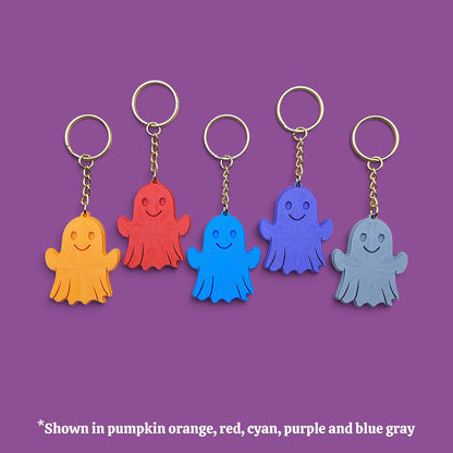 Five ghost-shaped keychains in different colors (orange, red, cyan, purple, and blue-gray) arranged in a row against a solid purple background, with a text note at the bottom indicating the color options.
