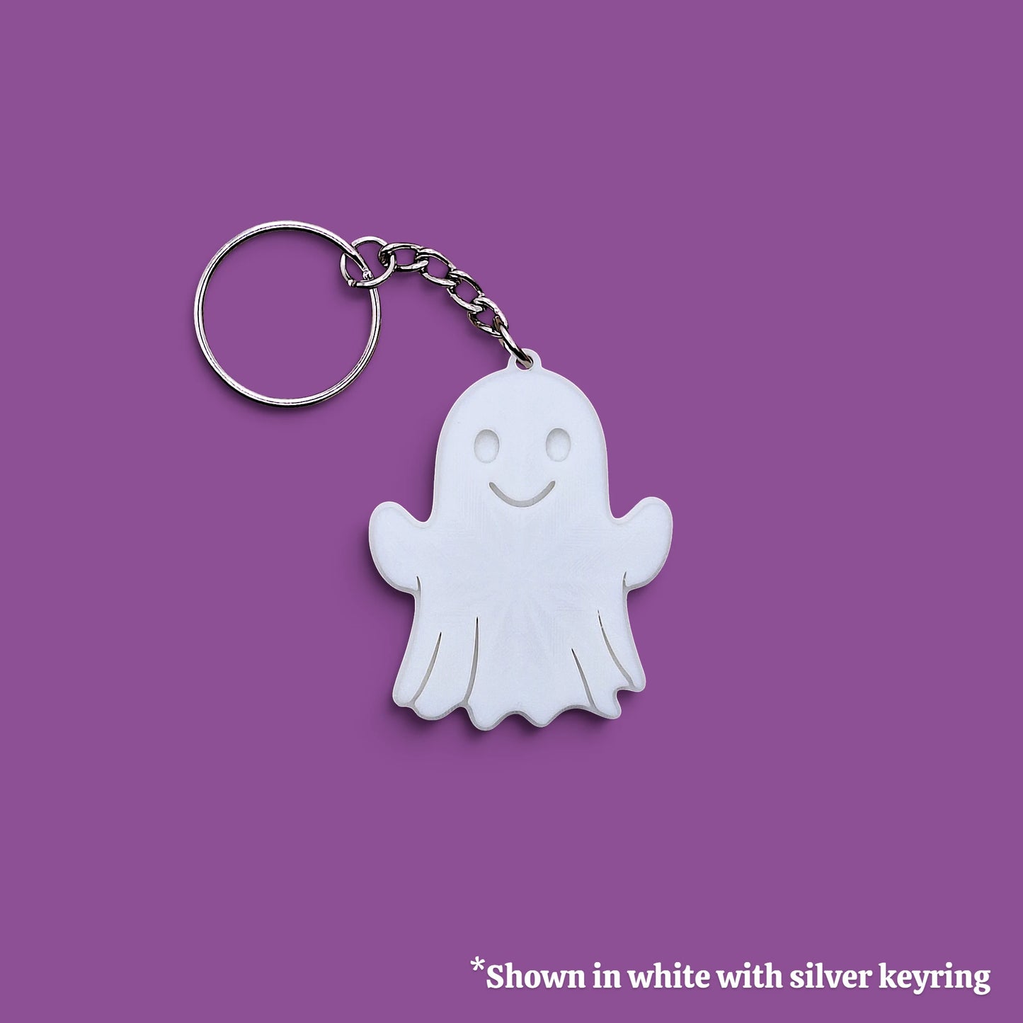 A white ghost-shaped keychain with a silver metal keyring and chain, shown on a solid purple background with a small text note at the bottom.