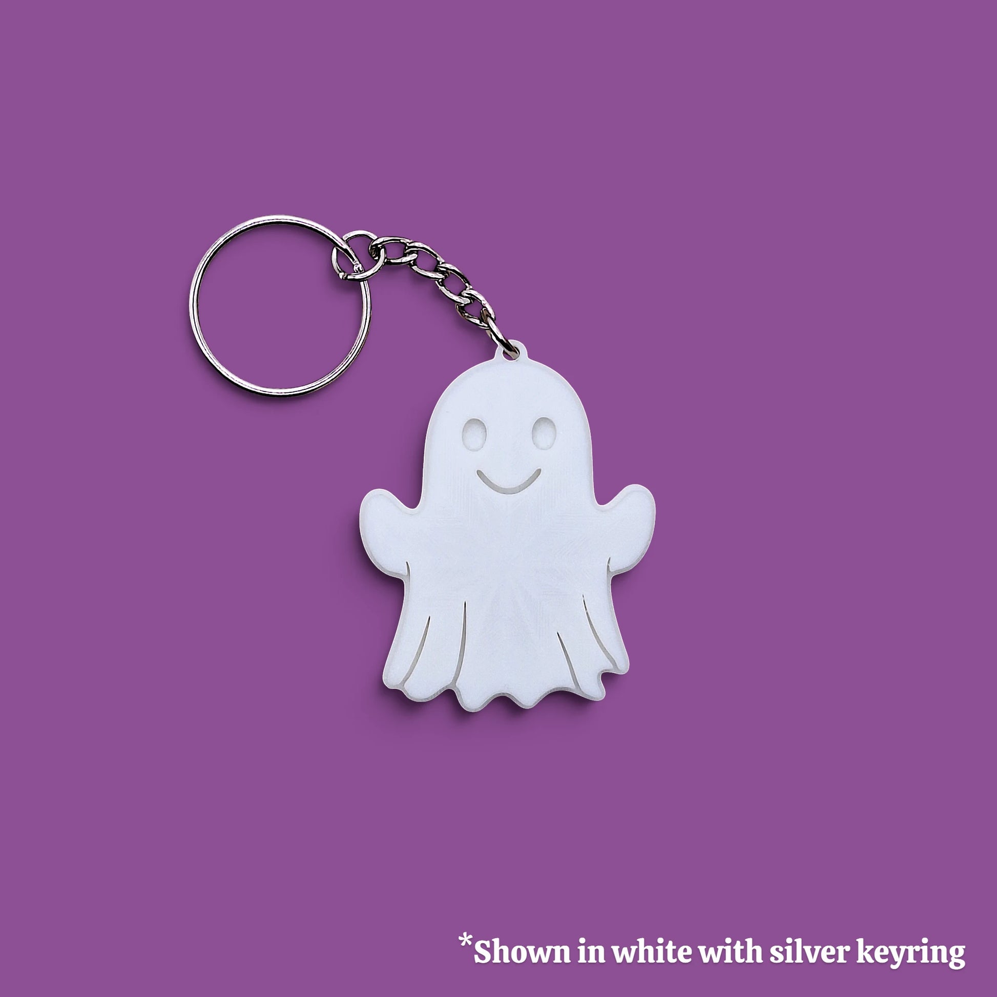A white ghost-shaped keychain with a silver metal keyring and chain, shown on a solid purple background with a small text note at the bottom.