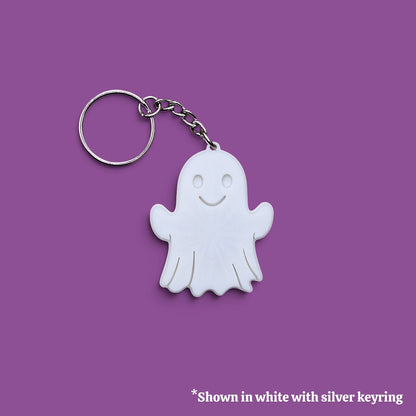 A white ghost-shaped keychain with a silver metal keyring and chain, shown on a solid purple background with a small text note at the bottom.