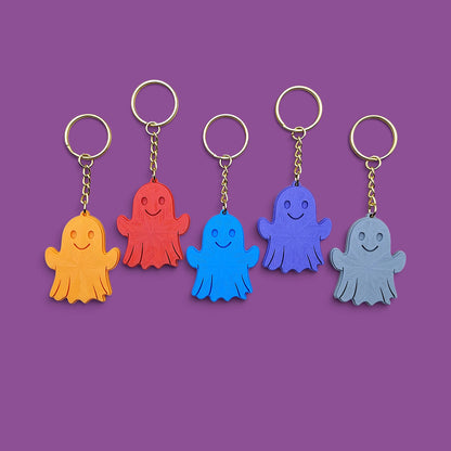 Five ghost-shaped keychains in orange, red, blue, purple, and gray, arranged in a row against a solid purple background.