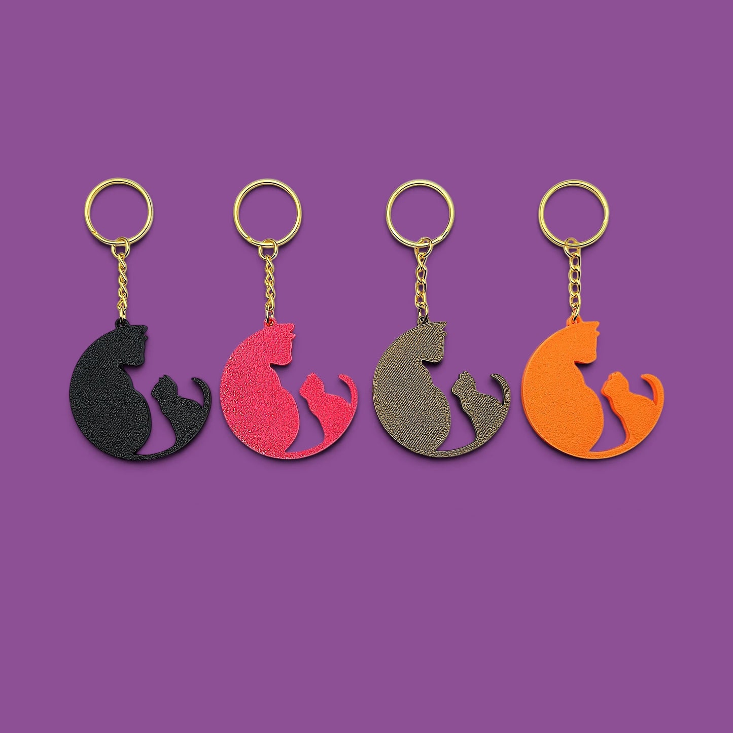 
Four cat-shaped keychains in different colors (black, magenta, bronze, and orange) arranged in a row on a solid purple background.