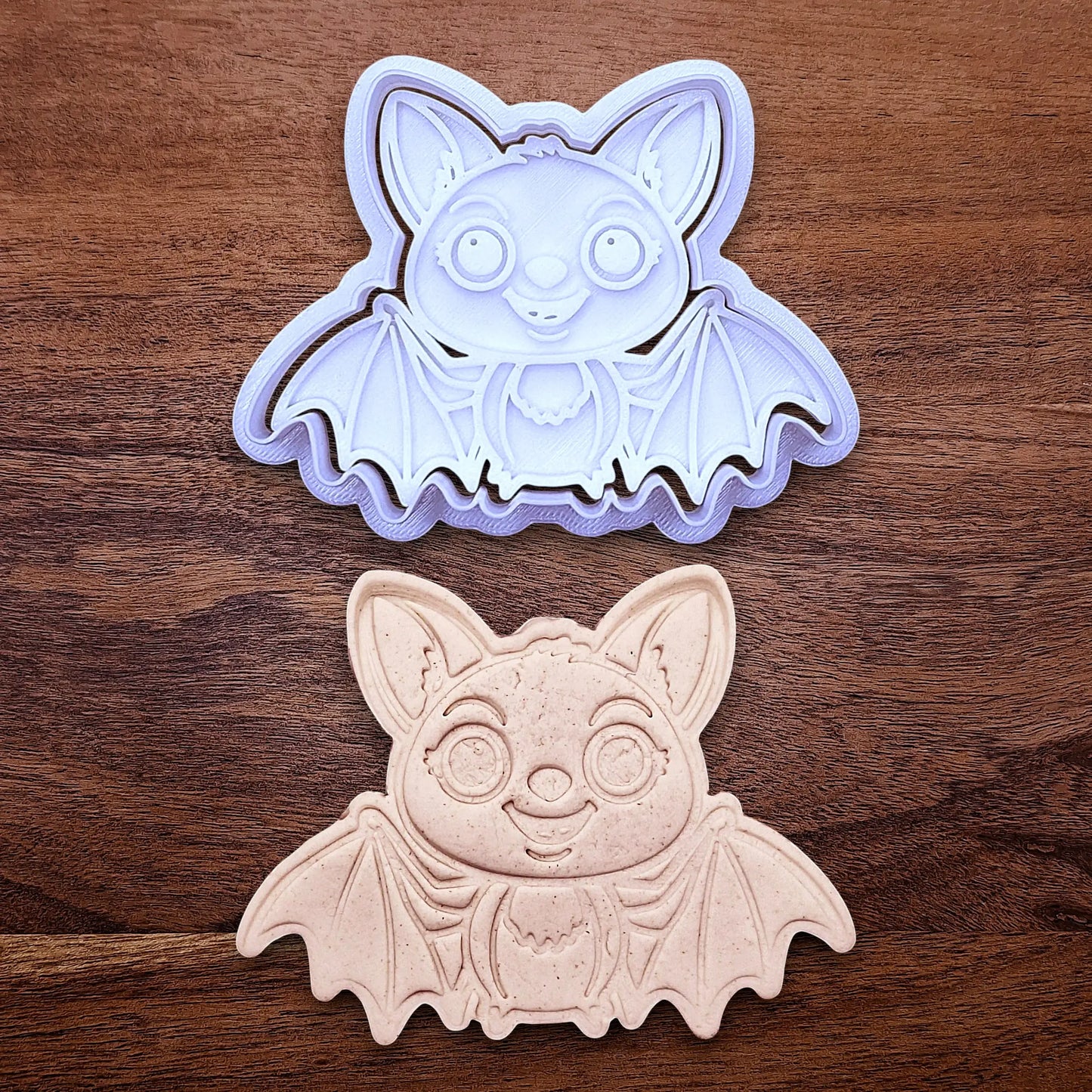 Cute bat cookie cutter with stamp alongside a dough cutout and imprint - adds cute Halloween charm, complete with cute details for whimsical baking, parties, or spooky gifting. Handmade and customizable in 30 colors.