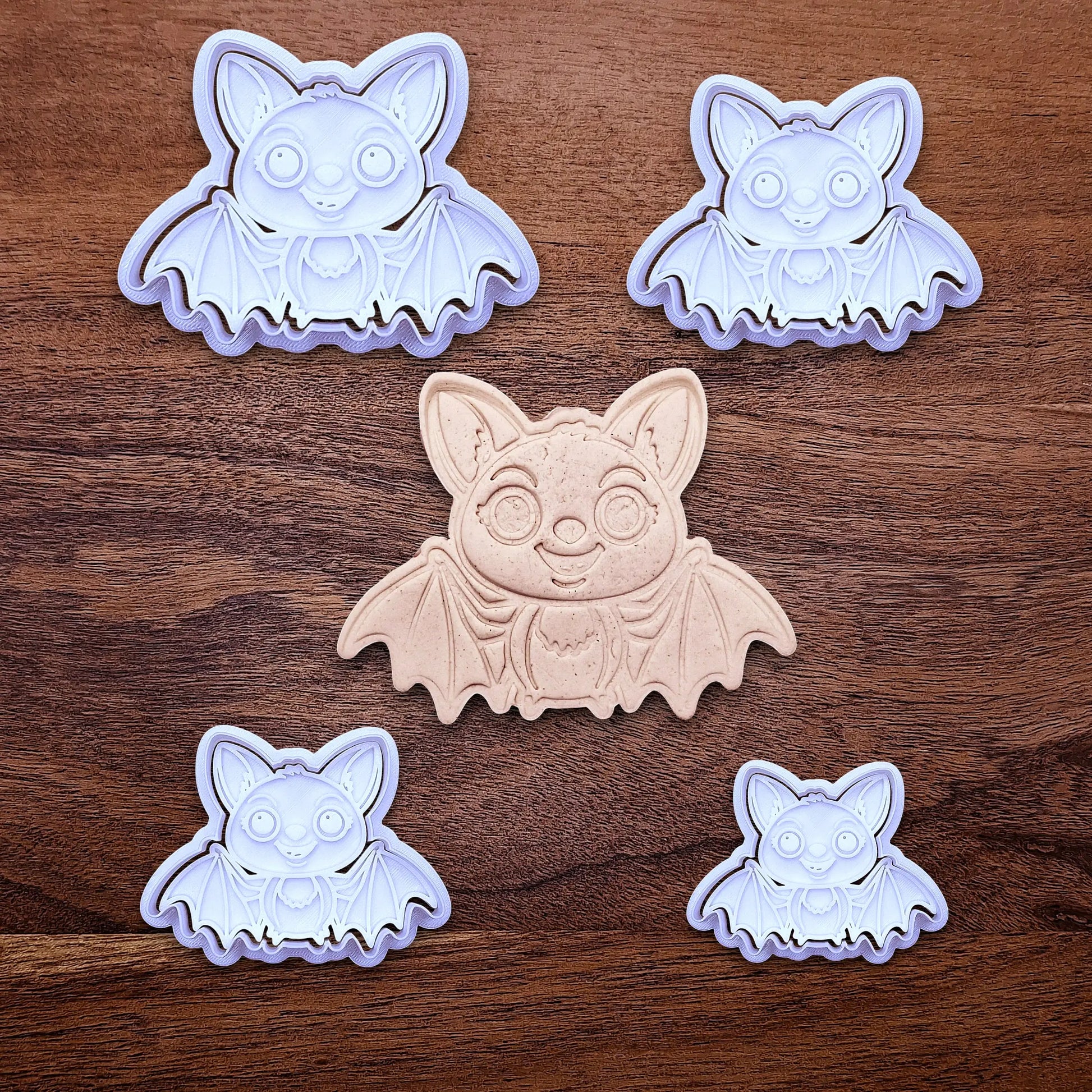 Multiple cute bat cookie cutters with stamps alongside a dough cutout and imprint - adds cute Halloween charm. Complete with cute details for whimsical baking, parties, or spooky gifting. Handmade and customizable in 30 colors.