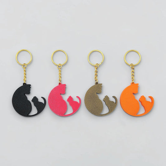 Four cat-shaped keychains in black, pink, brown, and orange on a light gray background.