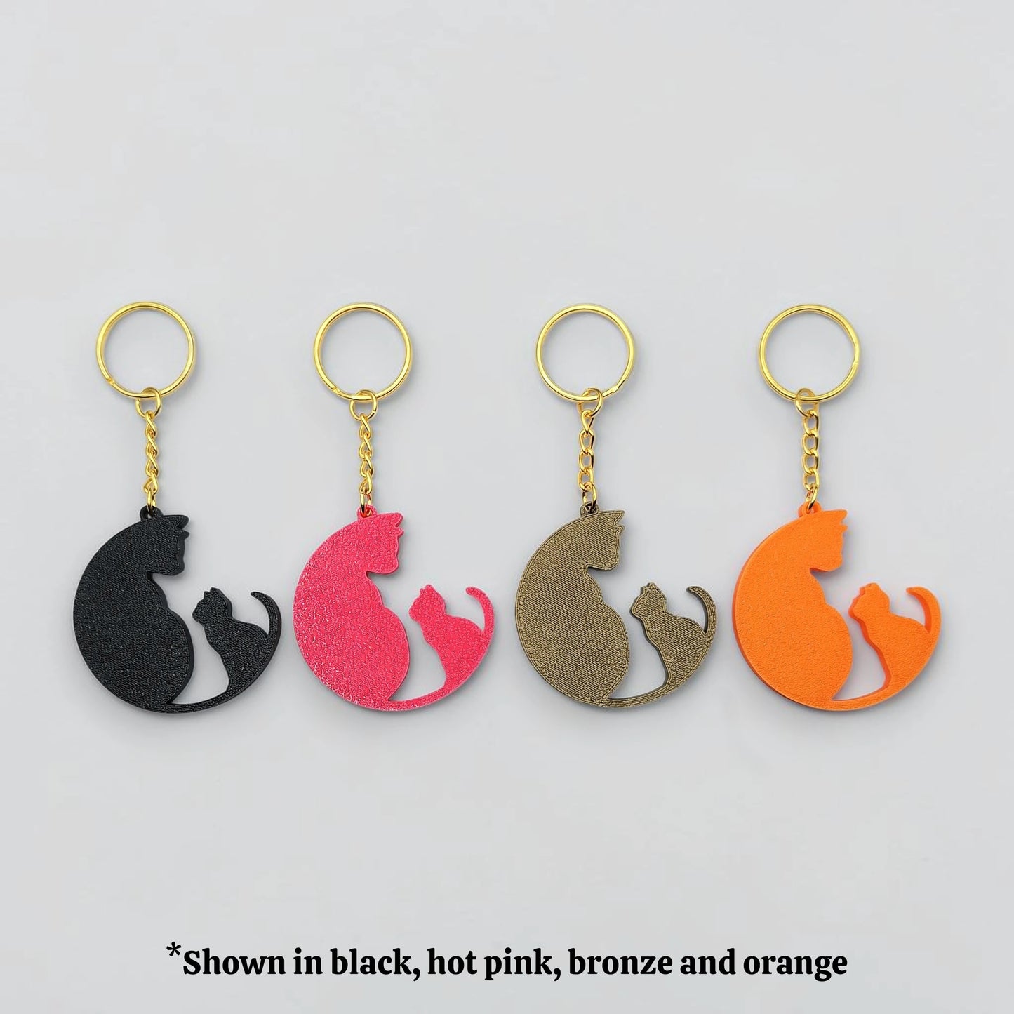 Four cat-shaped keychains in black, hot pink, bronze, and orange on a gray background.