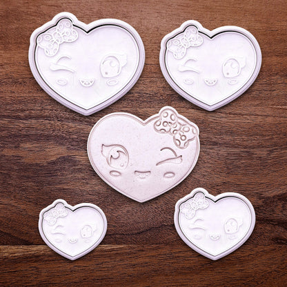 Heart cookie cutter set in various sizes with matching stamps and dough cutout—features cute winking face and bow design for sweet custom cookies.