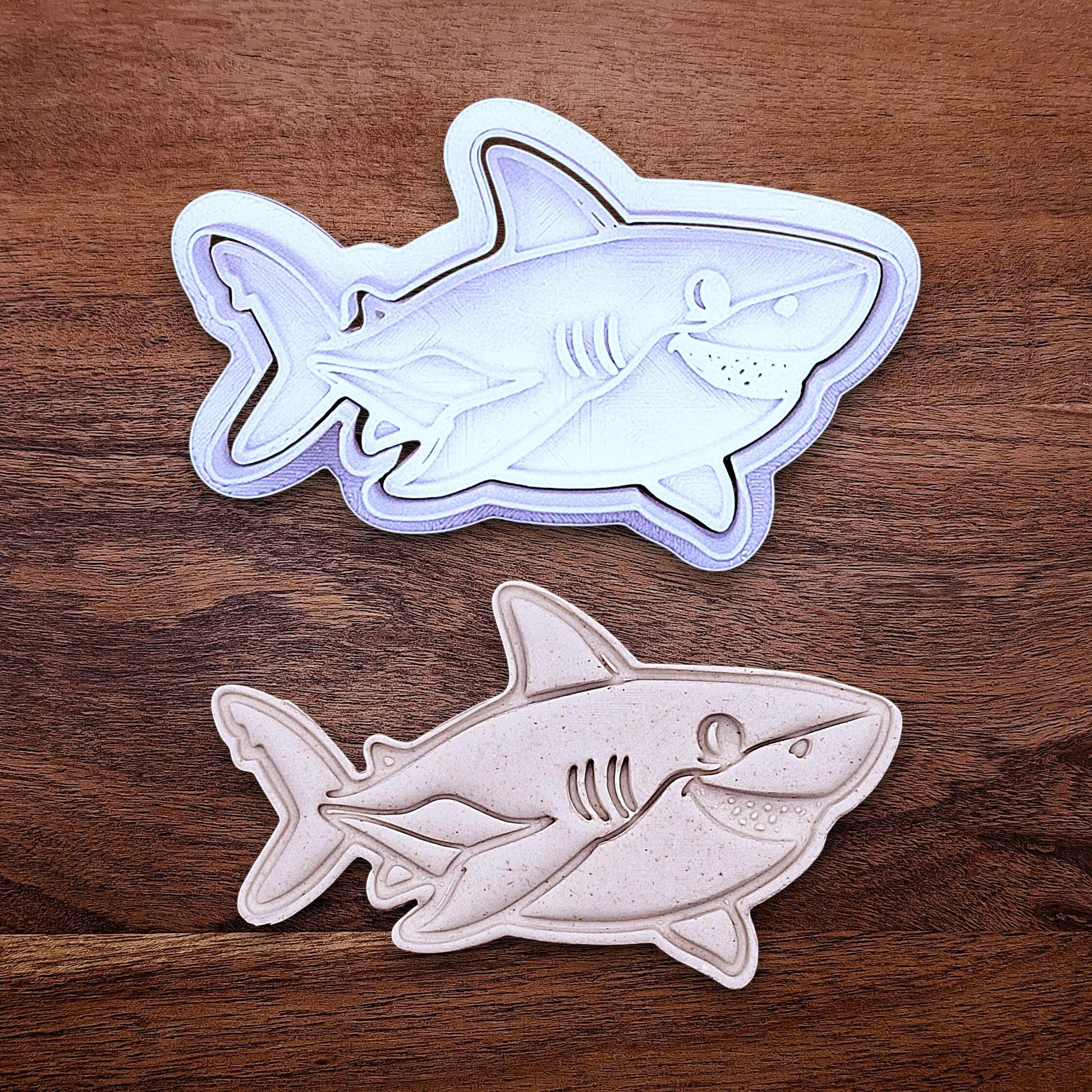 Customizable ocean shark cookie cutter and stamp above shark cutout and imprint, creates standout ocean cookies with charming face and fin details, perfect for themed birthdays, baby showers, and beach parties.