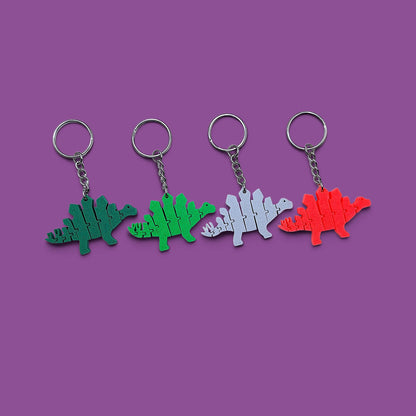 Four dinosaur-shaped keychains in green, light green, light gray, and red, arranged in a row on a solid purple background.