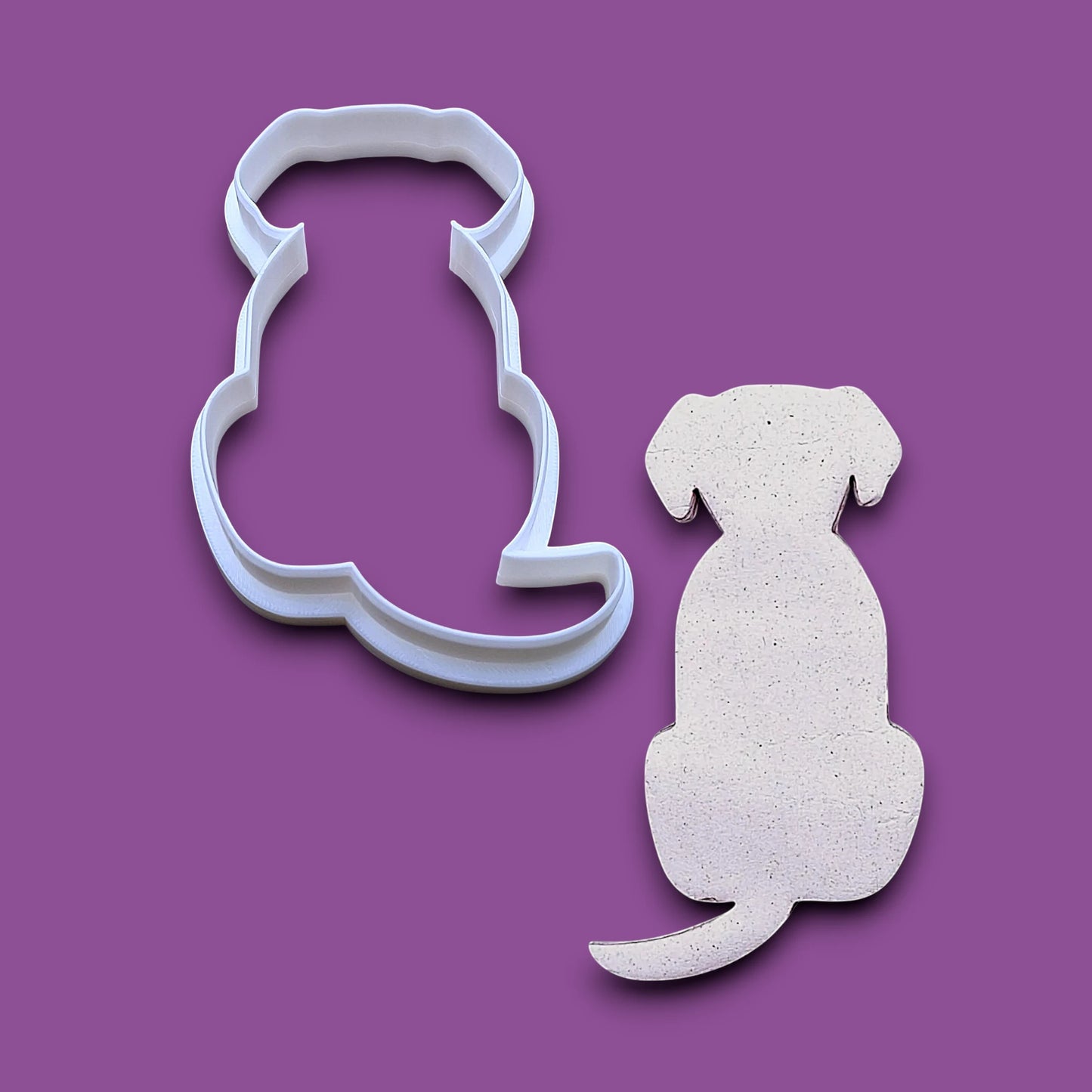 A dog-shaped cookie cutter and a matching dog-shaped cutout on a solid purple background.