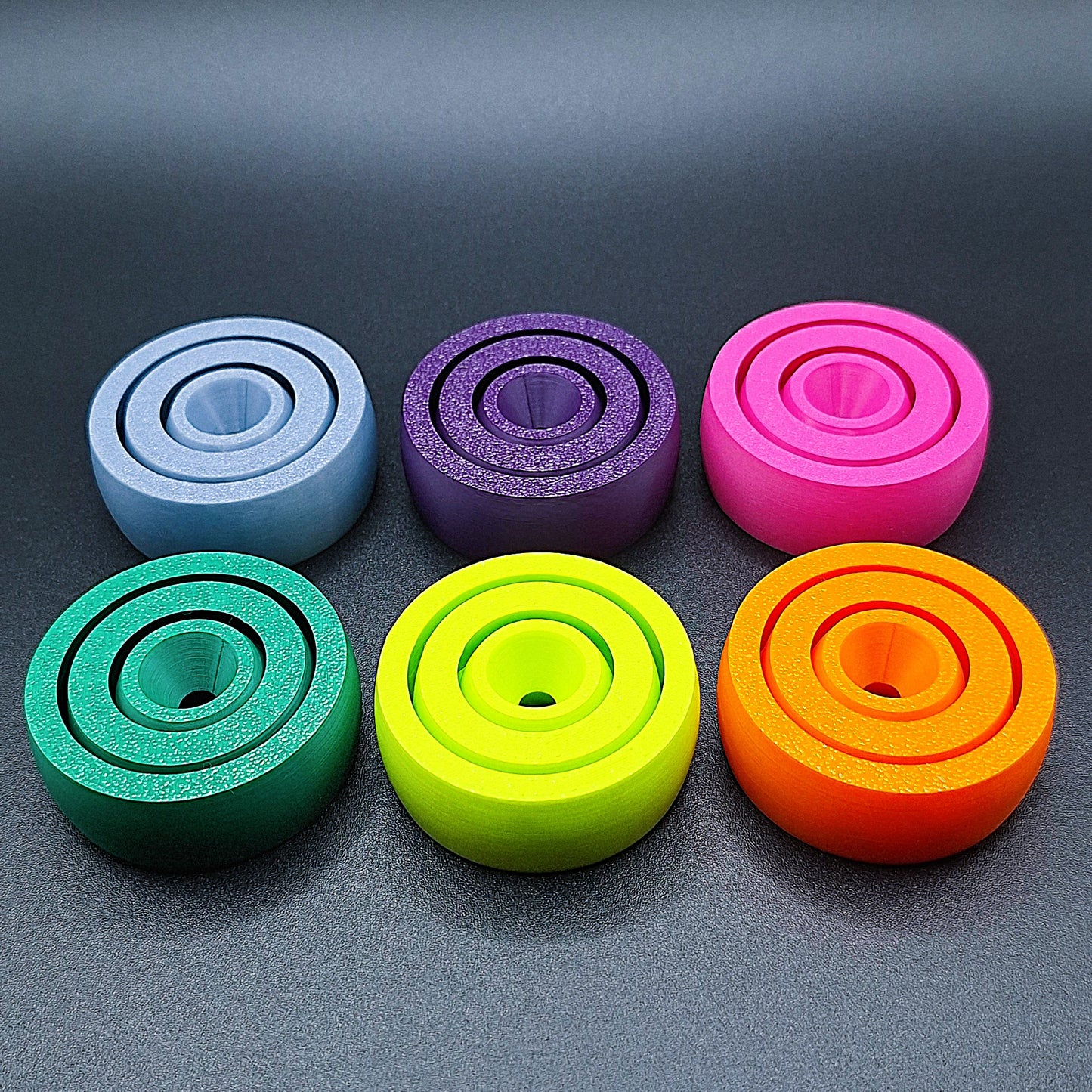 Front view of six smooth-surfaced fidget spinners in assorted colors, great for tactile calming, fidgeting, and mental focus.