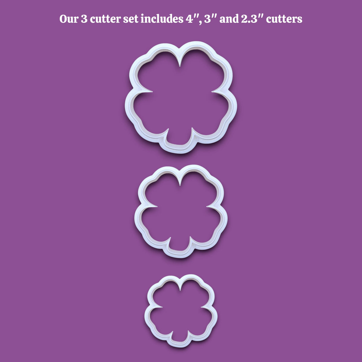 Three white four leaf clover shamrock  cookie cutters in sizes 4 inches, 3 inches, and 2.3 inches, displayed vertically on a solid gray background with black text at the top reading 'Our 3 cutter set includes 4", 3" and 2.3" cutters'
