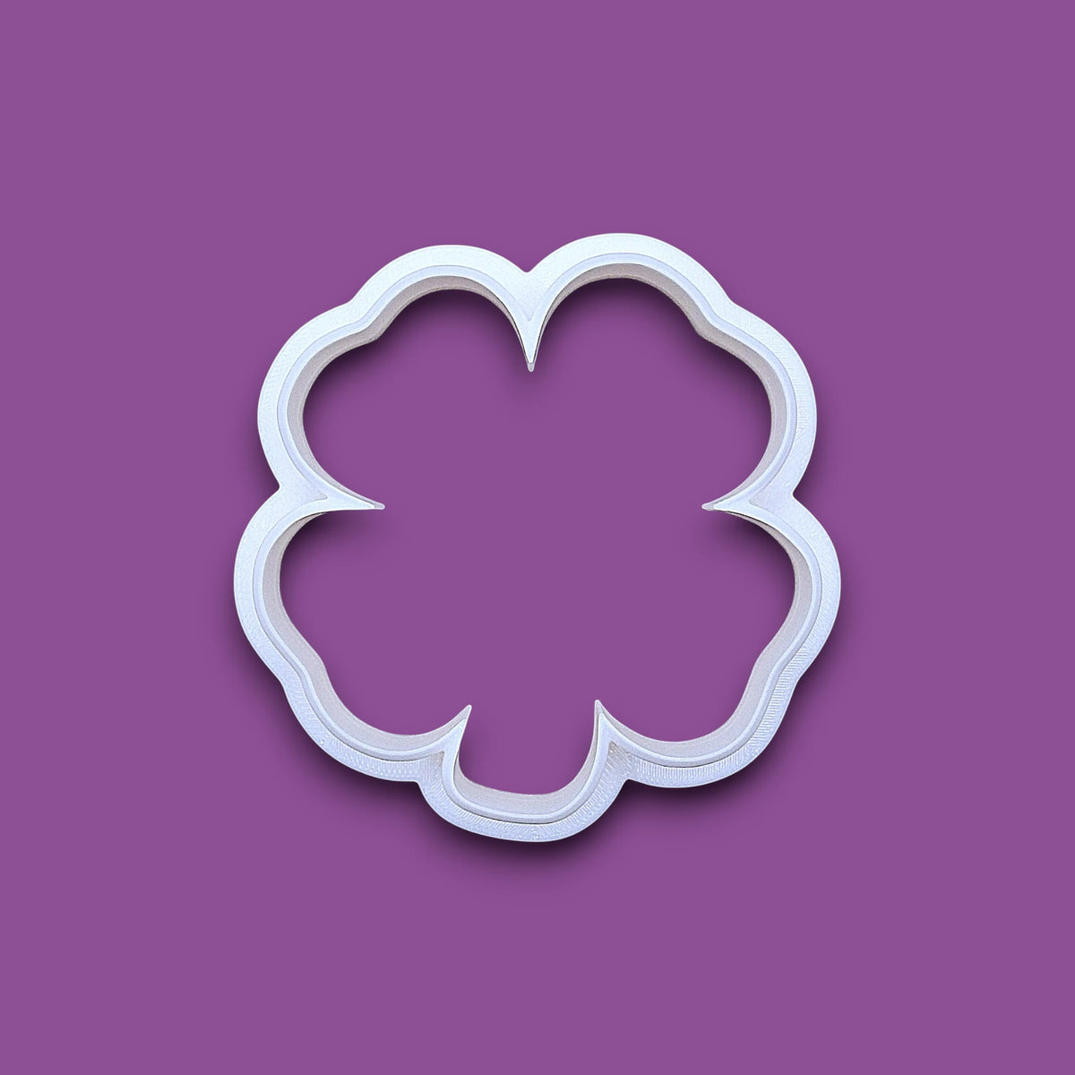 A white plastic four leaf clover shamrock cookie cutter, shown from a top-down perspective on a solid gray background.