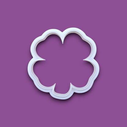 A white plastic four leaf clover shamrock cookie cutter, shown from a top-down perspective on a solid gray background.
