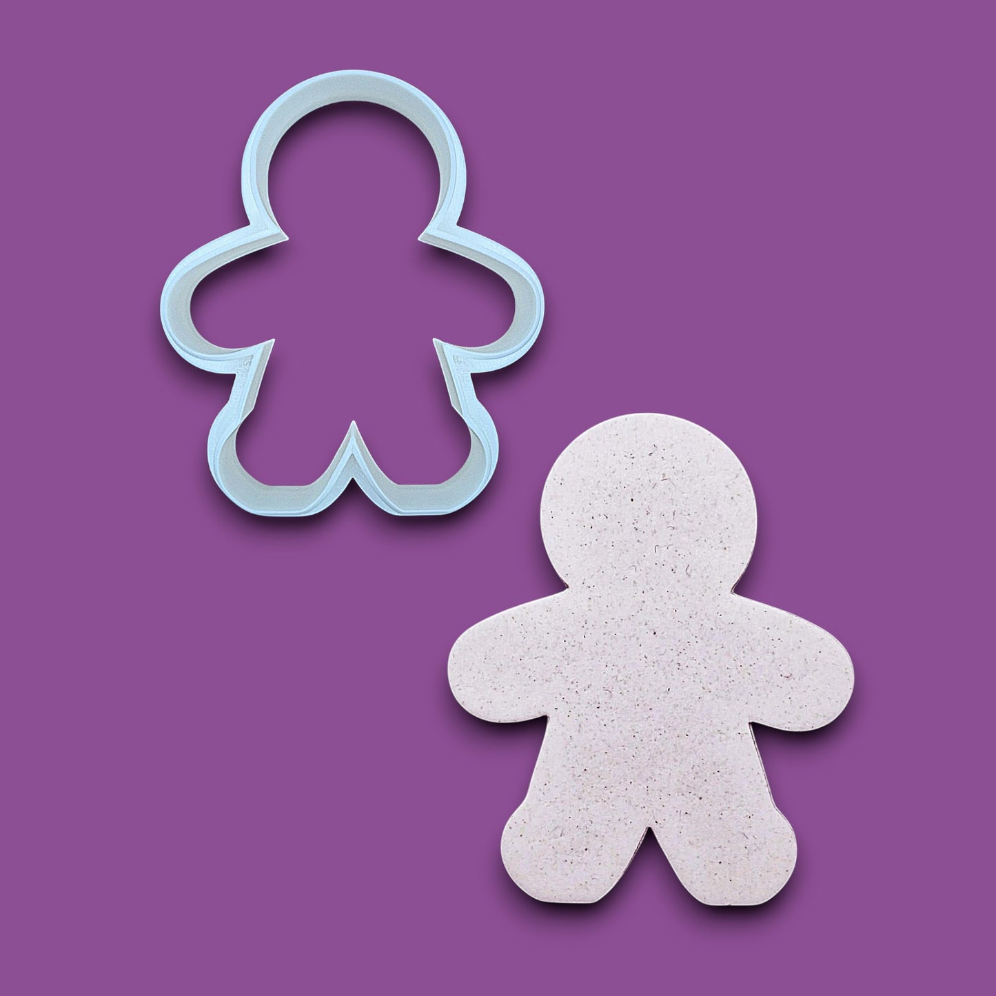 A white gingerbread man cookie cutter shown above a matching cutout of a gingerbread man made of speckled white cake mix, on a purple background.