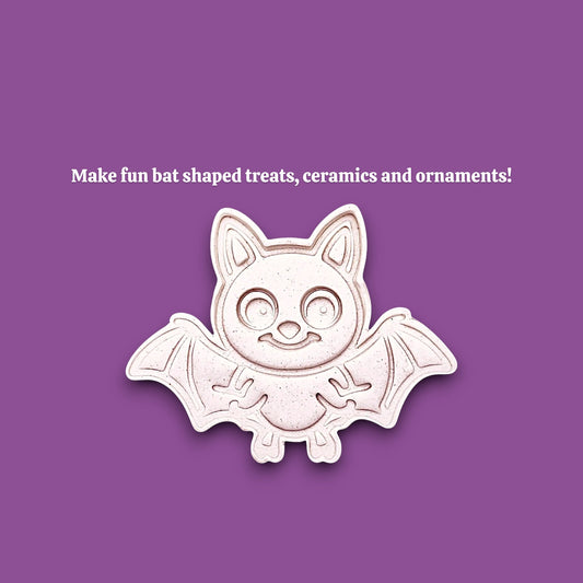 A cute bat-shaped cookie cutter mold shown on a solid purple background with white text that reads 'Make fun bat shaped treats, ceramics and ornaments!'. The bat is off-white with a light pinkish-beige undertone and a subtle drop shadow.