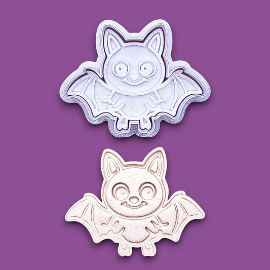 Bat cookie cutter with matching stamp alongside a dough cutout and imprint, perfect for spooky Halloween cookies, fondant crafts, and gothic-themed baking projects.