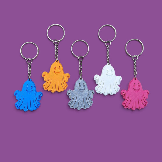 Five plastic ghost keychains in blue, orange, gray, white, and pink, arranged in a row on a solid purple background.