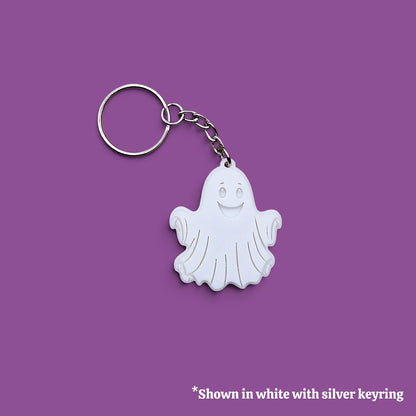 A ghost-shaped keychain charm in white with a silver metal keyring and chain, shown on a solid purple background with a small text note at the bottom.