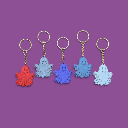 Five ghost-shaped keychains in red, light blue, dark blue, and pale blue, arranged in a row on a solid purple background.