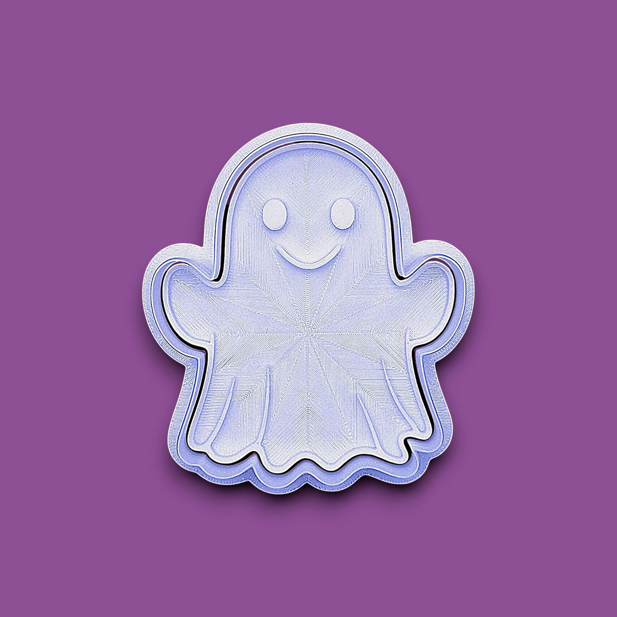 A ghost-shaped cookie cutter or stamp with a smiling face, shown on a solid purple background.