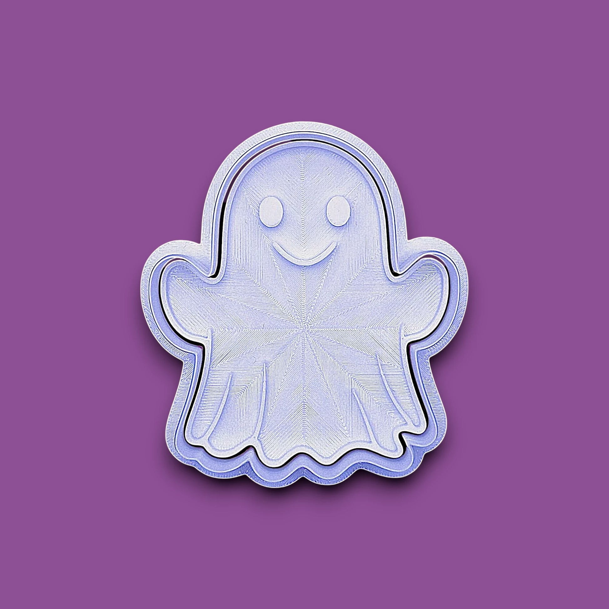 A ghost-shaped cookie cutter or stamp with a smiling face, shown on a solid purple background.