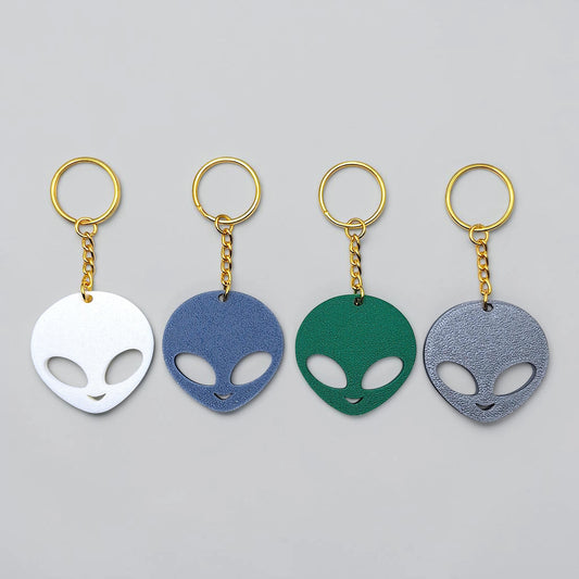 Four alien head keychains in white, blue, green, and gray on a gray background