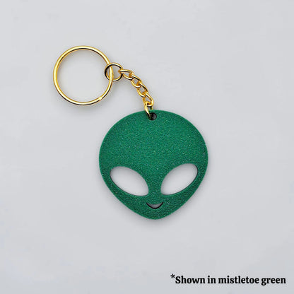 Green alien head keychain with gold ring on a light gray background