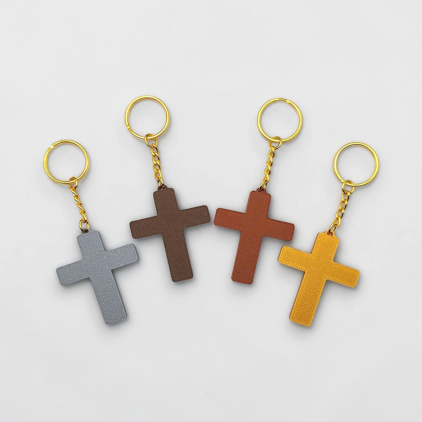 Four cross-shaped keychains in gray, brown, red, and yellow on a light gray background.