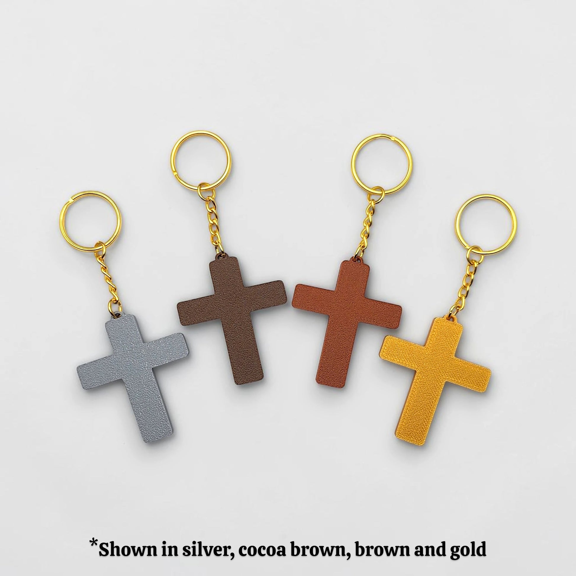 Four cross-shaped keychains in silver, cocoa brown, brown, and gold on a gray background.