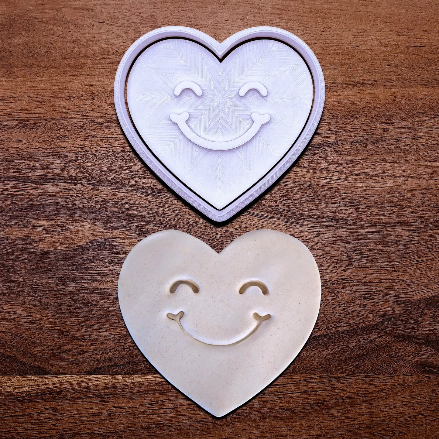 Handmade and customizable heart cookie cutter and stamp with cute face stamp alongside a dough cutout and imprint, perfect for Valentine's Day baking, sweet treats and party favor creations.