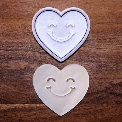 Handmade and customizable heart cookie cutter and stamp with cute face stamp alongside a dough cutout and imprint, perfect for Valentine's Day baking, sweet treats and party favor creations.
