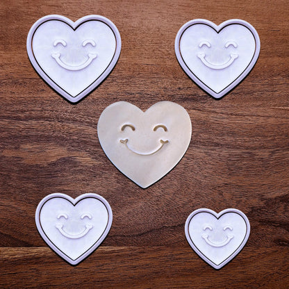 Handmade and customizable heart cookie cutters and stamps with cute face stamp alongside a dough cutout and imprint, perfect for Valentine's Day baking, sweet treats and party favor creations.