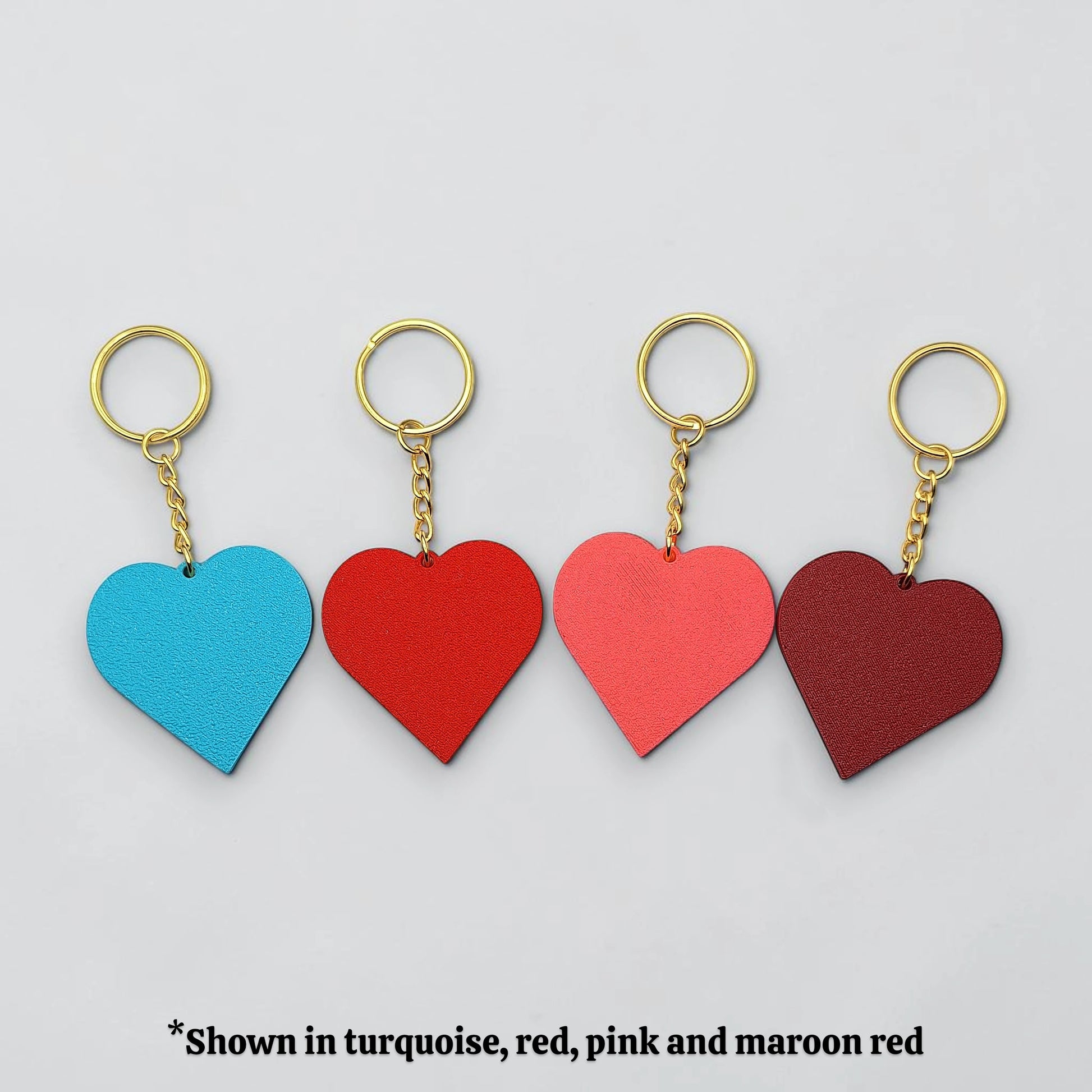 Four heart-shaped keychains in turquoise, red, pink, and maroon on a light gray background.