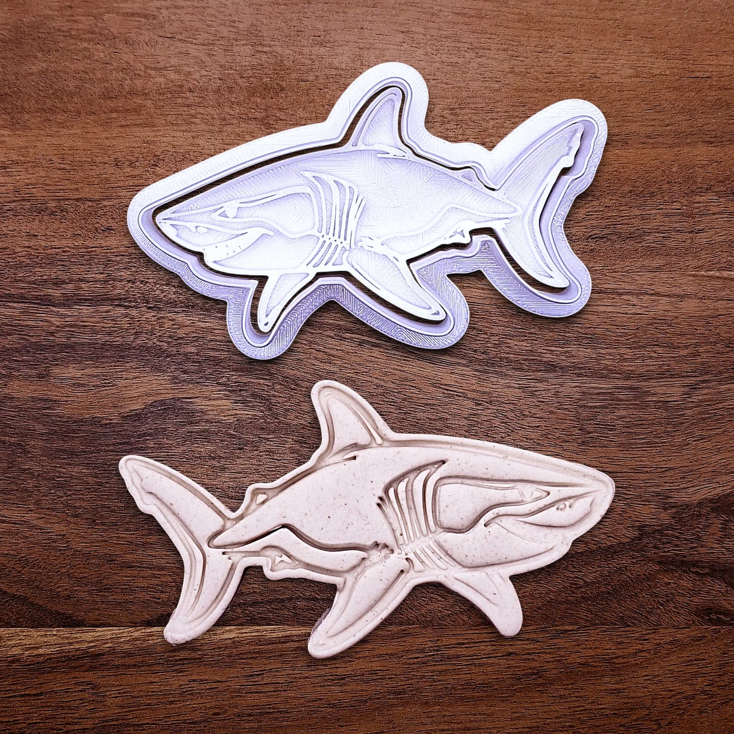 Handmade and customizable shark cookie cutter and stamp alongside a dough cutout and imprint, great for beach themed baking, fondant crafts, or ocean-themed cookies.