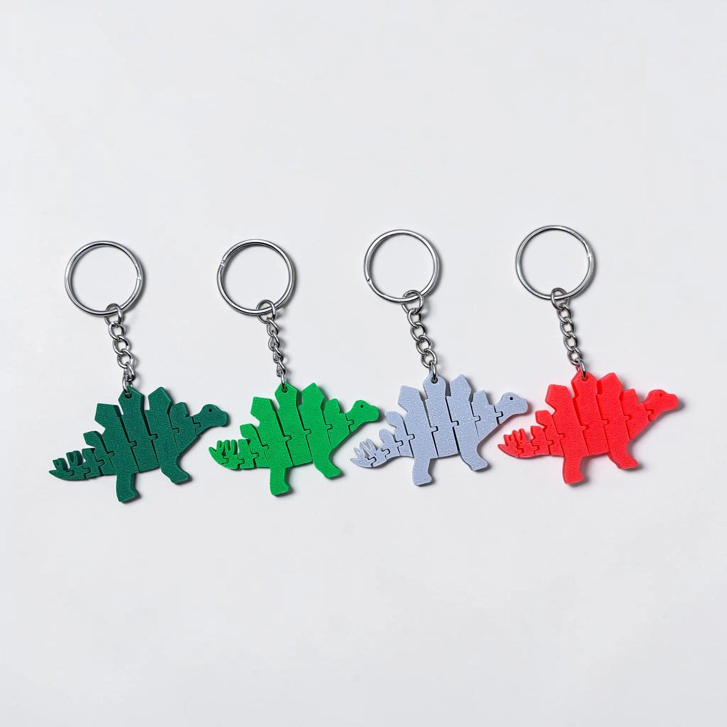 Handmade and customizable dinosaur fidget keychains in various colors, featuring colorful articulated designs, perfect for kids birthday parties, classroom prizes, sensory play, and party favor dino gifts.