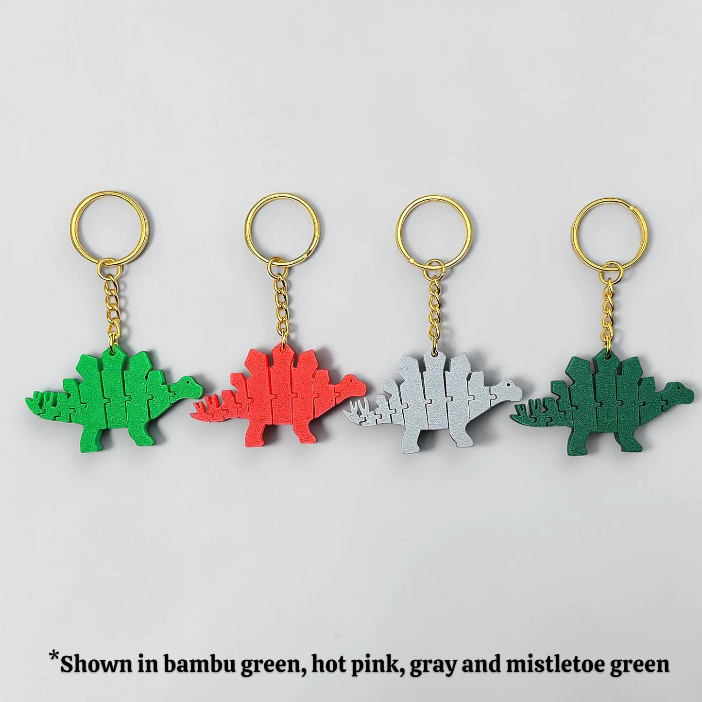 Four dinosaur-shaped keychains in different colors on a light gray background