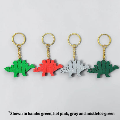 Four dinosaur-shaped keychains in different colors on a light gray background